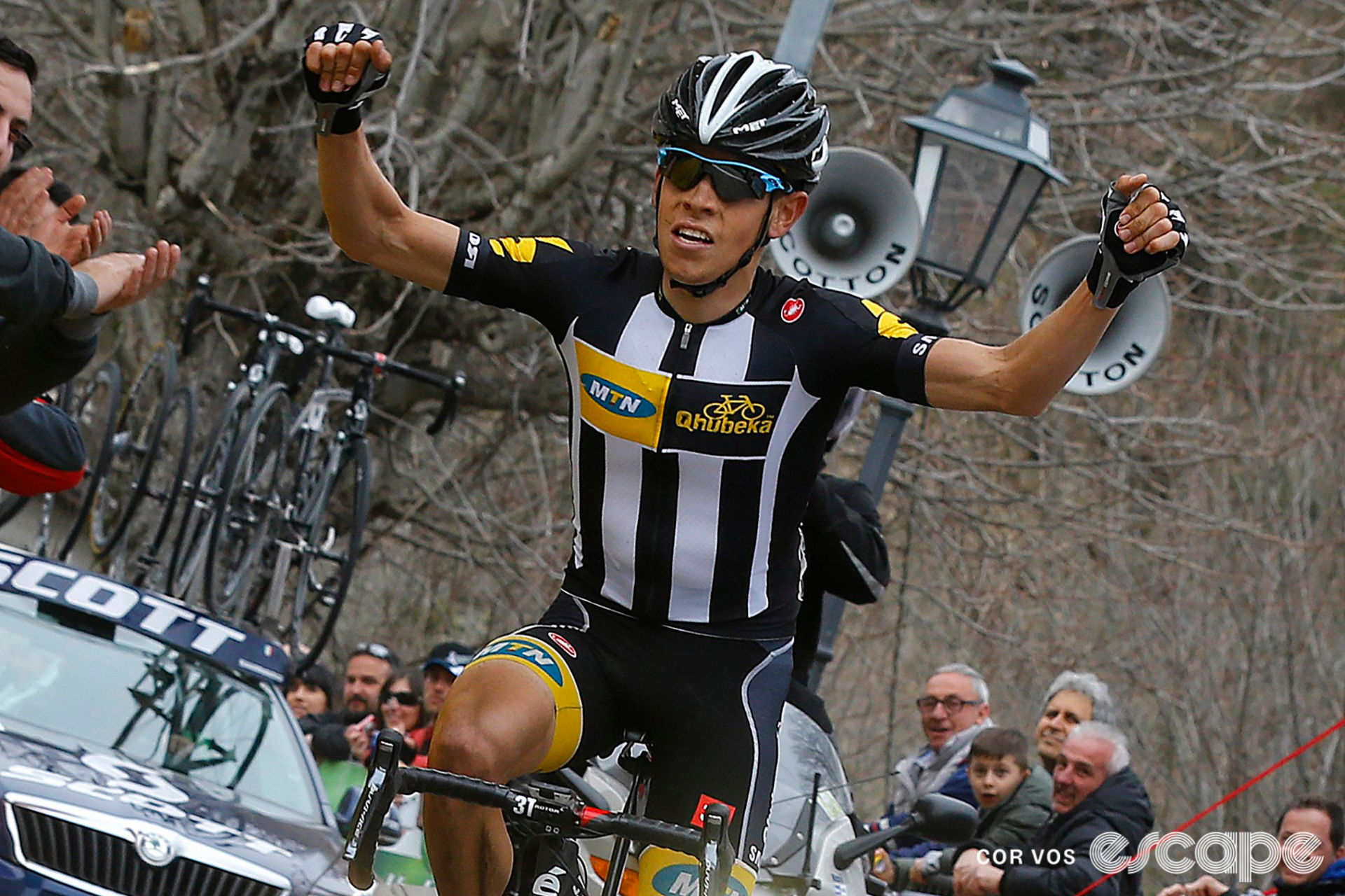 Louis Meintjes raises both arms in victory wearing the vertical black and white striped era MTN-Qhubeka kit.