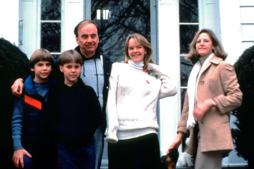 A man, a woman, and three teens pose together outside a house