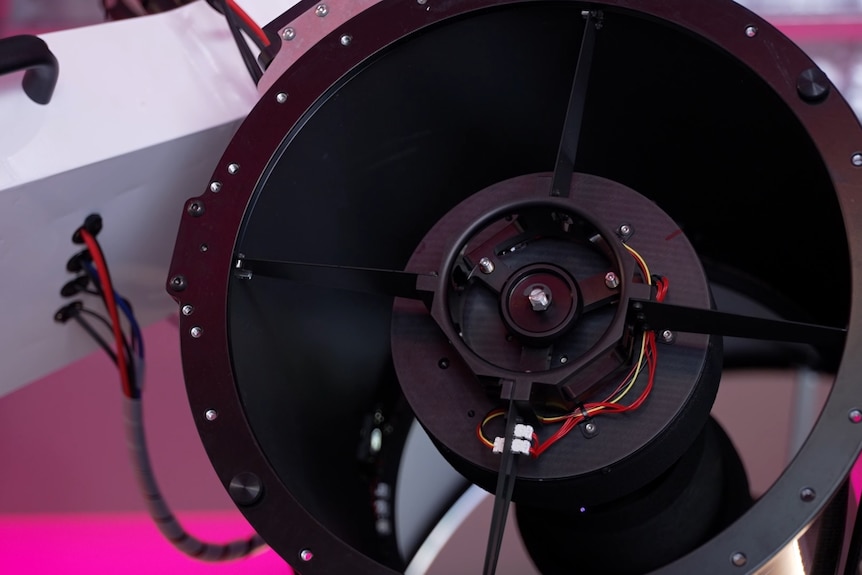 An up close of a telescope camera, with pink lights in the background.