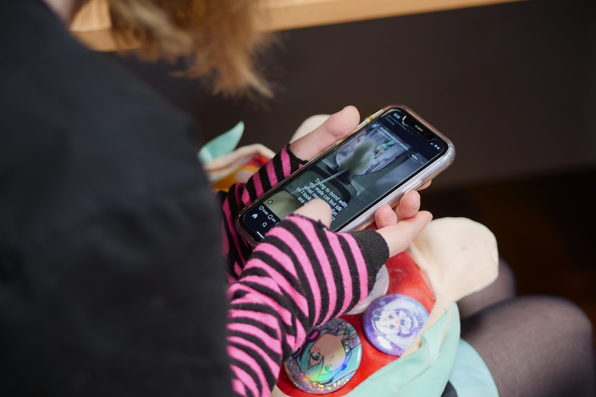 Kelsey Van der Woude scrolls on her phone. She's wearing pink and black striped fingerless gloves.