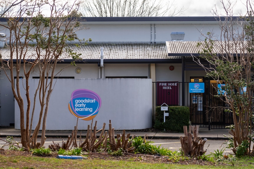 a grey sign with a blue logo for a childcare centre against a blue sky and green grass