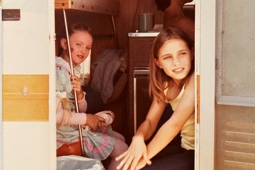 A trailer door is open and two kids sit inside.