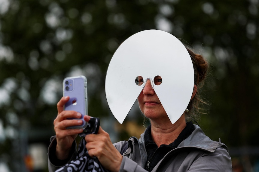 A woman wears a moon shaped plate over her face while taking pictures.