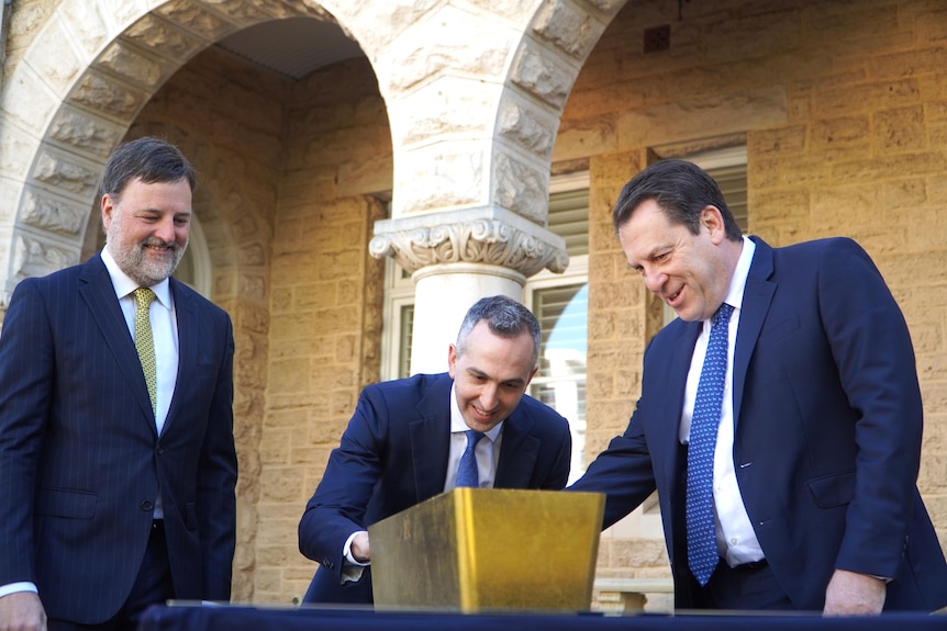 A huge gold bar is on display with three men looking at it.