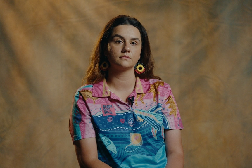 A young woman with brown hair stares at the camera