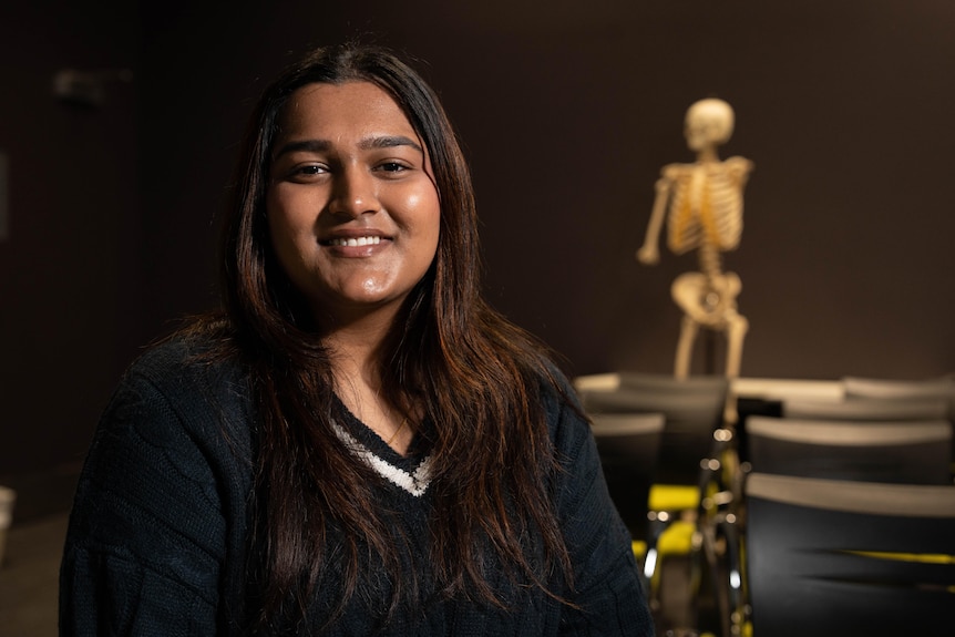 A woman smiles for the camera, with a skeleton pictured in the background.