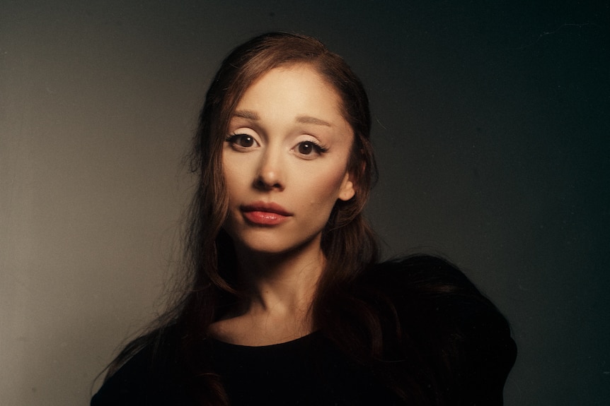 Ariana Grande with long brown hair, and slight frame wearing black.