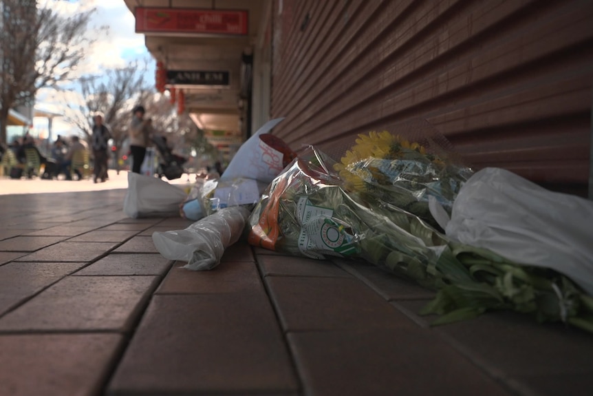 A photo taken from ground level of bouquets of flowers lying on a brick surface against a red roller door.