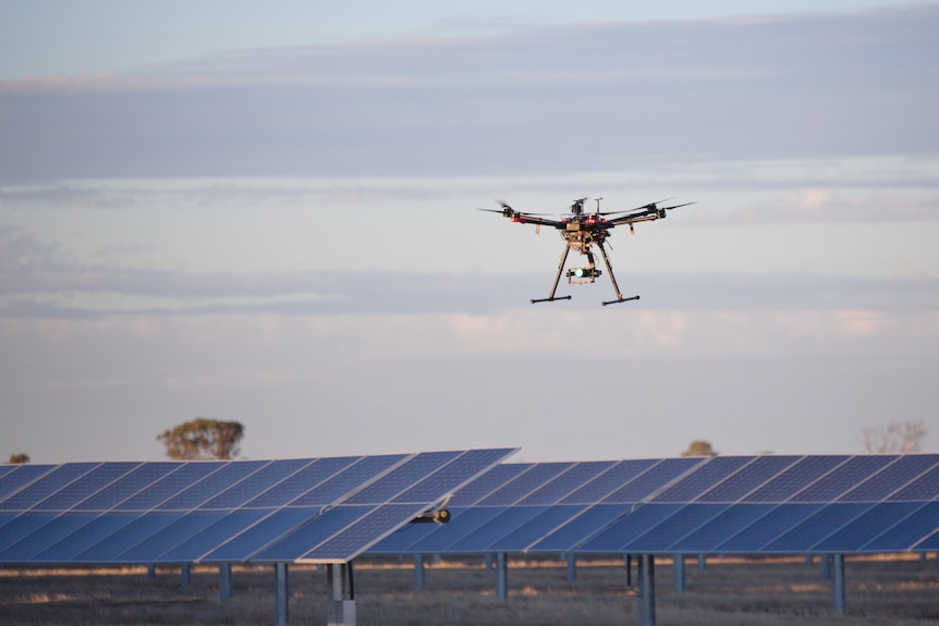 A drone hovers low over a field of solar panels, date and location unknown.