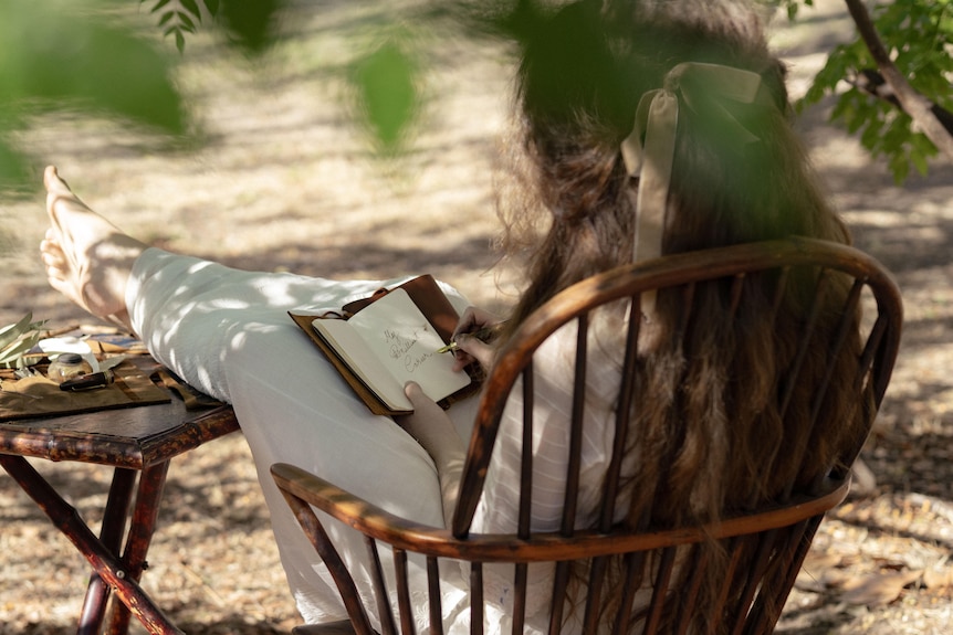 A woman sitting on a chair with legs on table holding a book in hands