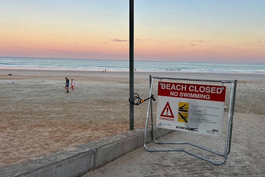 A crocodile warning sign on a beach. The sign reads "Beach closed no swimming".