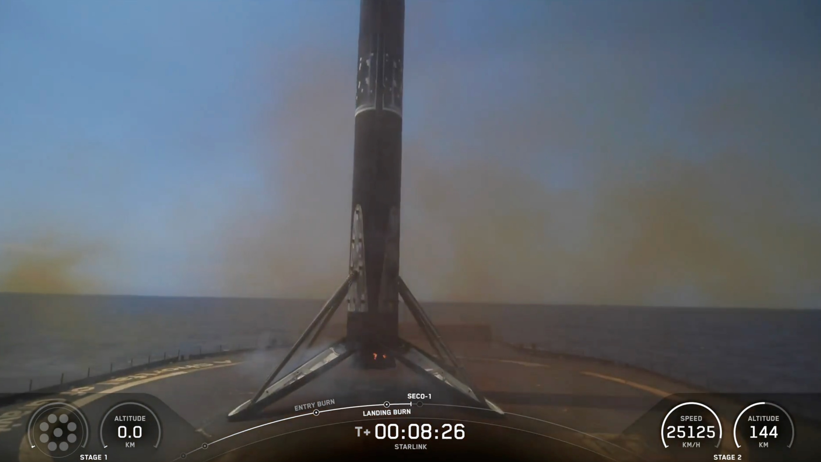 A black and white spacex falcon 9 rocket first stage sits on the deck of a ship at sea.