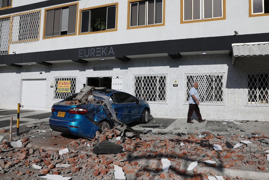 Bricks and debris fallen on a car out the front of a building.