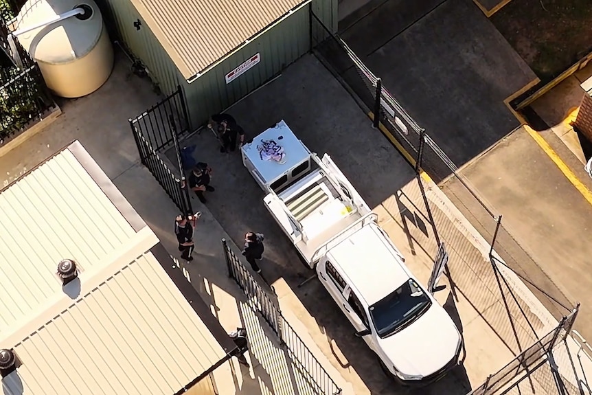 An aerial shot of an outdoor warehouse-looking facility with a council vehicle and four council workers surrounding the boot.