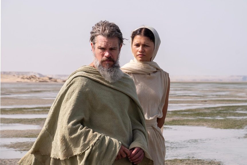 Athena (Zendaya) assists Odysseus (Matt Damon) stand on a land flat