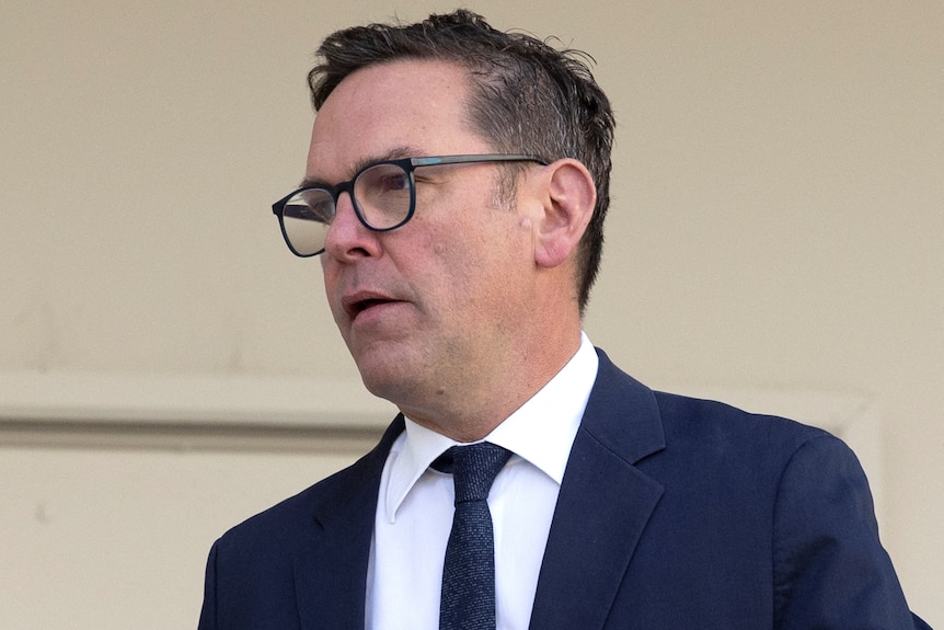James Murdoch walks outdoors in front of a white wall.