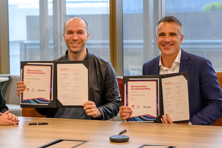 The men hold up certificates while sitting at a table