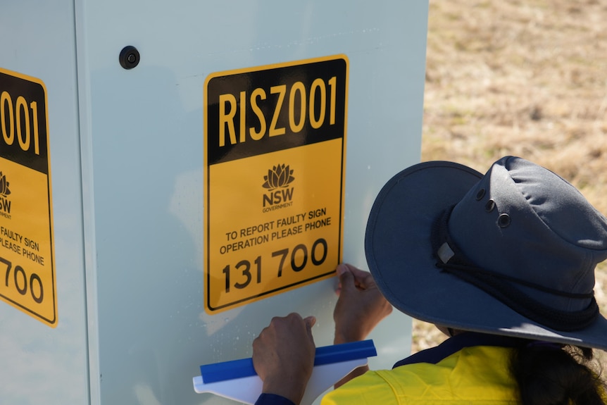 A person in high vis applied a yellow and black sticker to an electrical unit which reads RISZ001