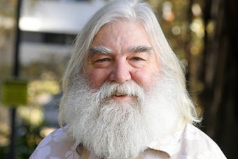 A man with long white hair and beard smiles at the camera.