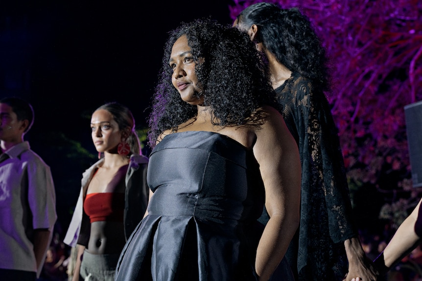 Natisha Tabua front and centre of a crowd of people, wearing a black satin strapless top with her black curly hair styled.