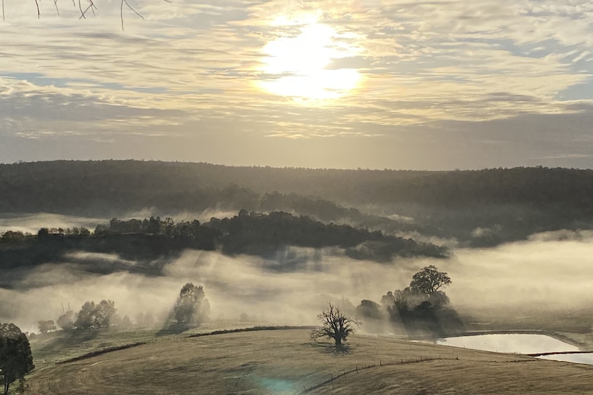 Mist and fog blankets low-lying areas of Ferguson Valley with the sun behind clouds in the sky.