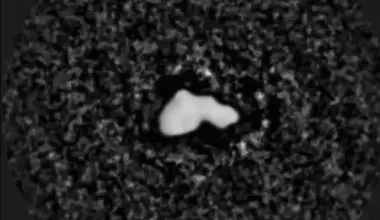 A lumpy white rock on a dark grainy background spins and one brighter dot at upper left circling it.