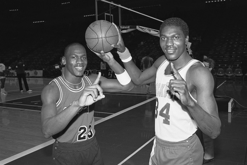 Michael Jordan and Hakeem Olajuwon hold a ball