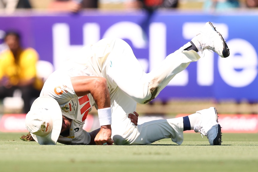 A cricketer in white rolls while catching the ball