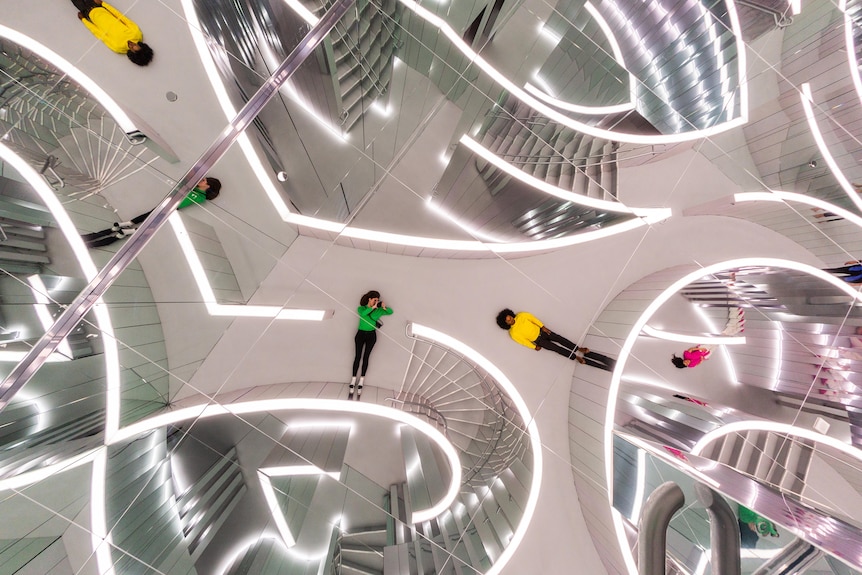 Two children lie flat on the ground inside a labyrinth of mirrors