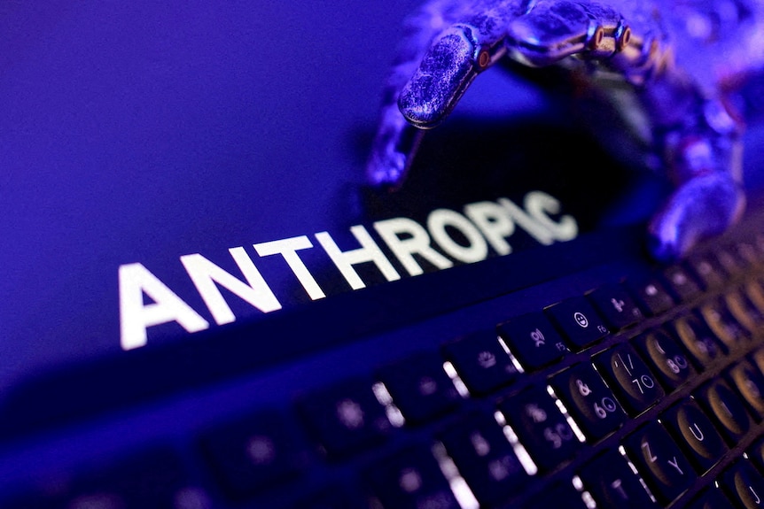 A screen showing an Anthropic logo is displayed next to a keyboard and a blue robotic hand.