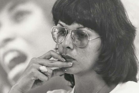 A black and white photo of Pat Turn as a young woman with large aviator glasses on. She has her hand up near her mouth.
