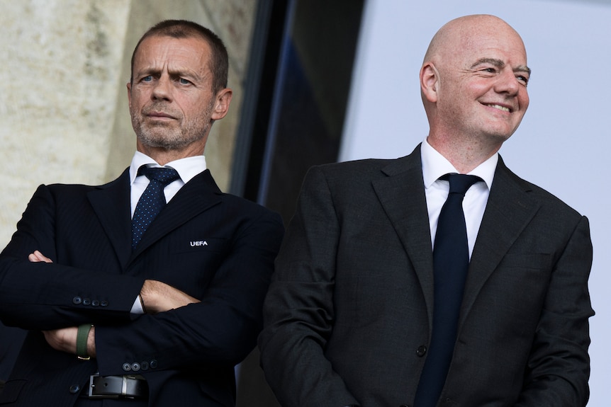 Two men watch on from the stands during a football match.