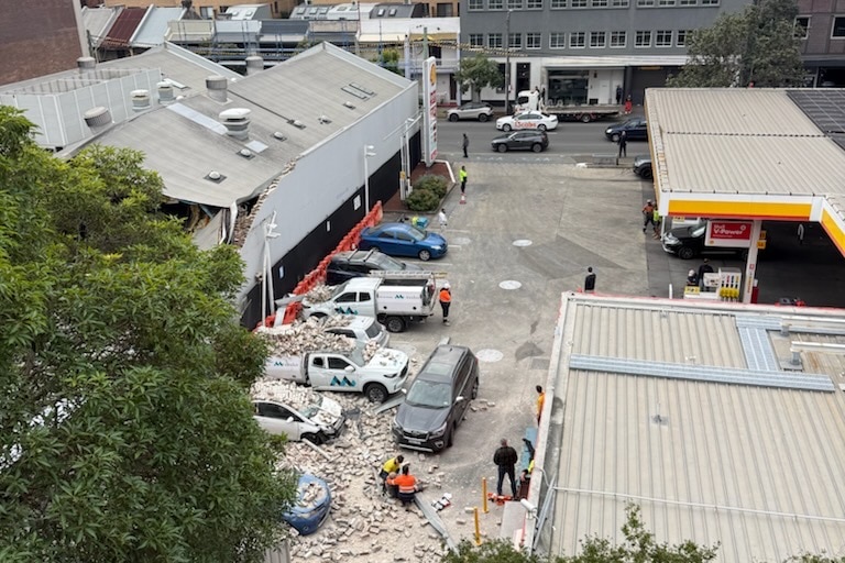 At least three cars parked next to a building with rubble and bricks on them.
