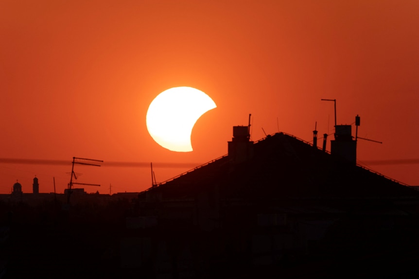 The moon covers the sun behind a house roof.