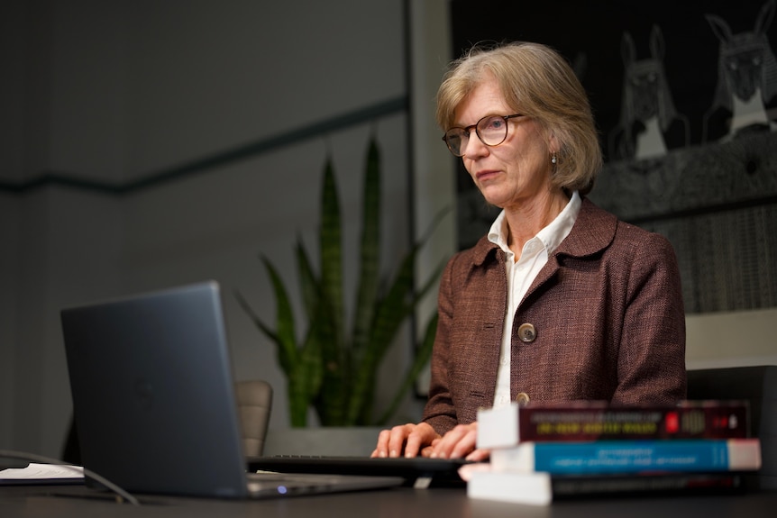 A woman sits at a desk typing on a laptop.