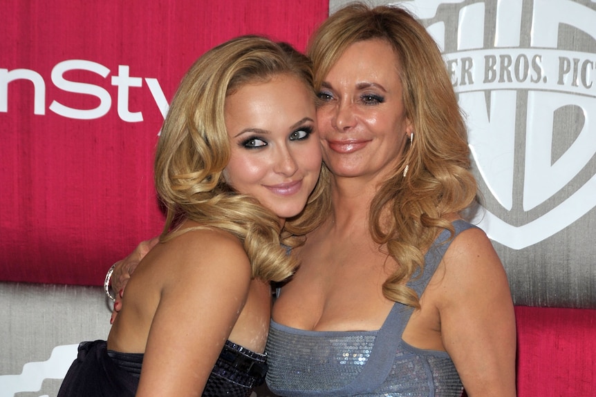 Two women pose in figure-hugging dresses on a red carpet.