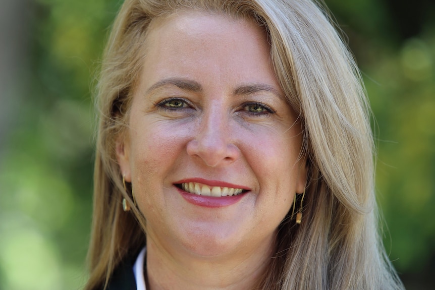 A woman with blonde hair in a headshot with leafy green background