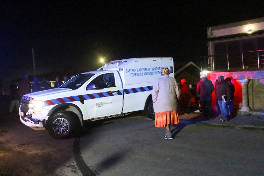 A forensic pathology vehicle parked outside a home. People surround it. 