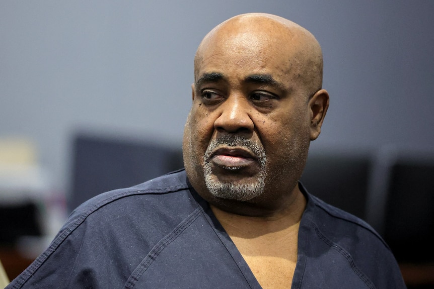 A man grey-blue jail clothing looks to his right