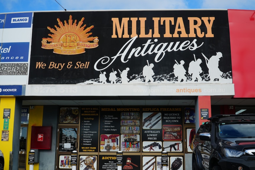 A shopfront is topped with a black sign with "military antiques" written in large font and silhouettes of sold