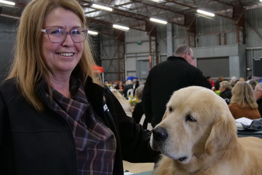 A woman smiling at the camera patting a golden retriever dog