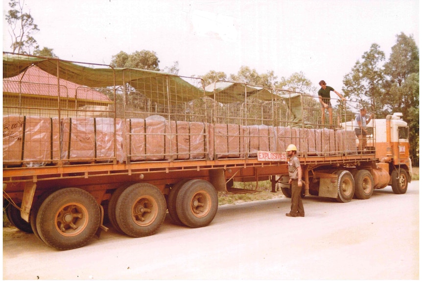 A old grainy photo of a long flat-bed truck loaded with crates with a person beside it and on top.