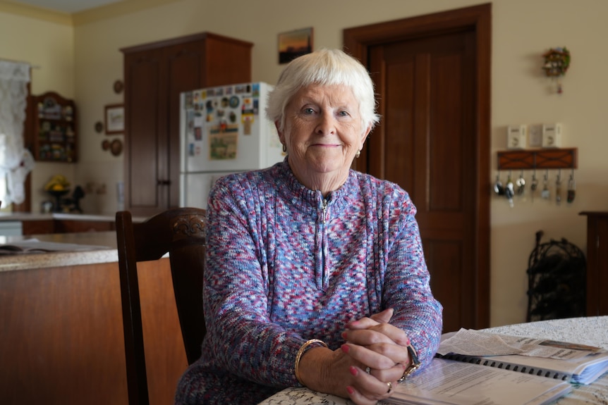 A woman sitting at a table with her hands folded.