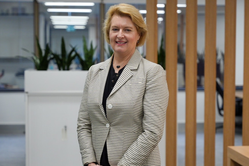 Woman swearing a suit standing in the middle of an open plan office, smiling.