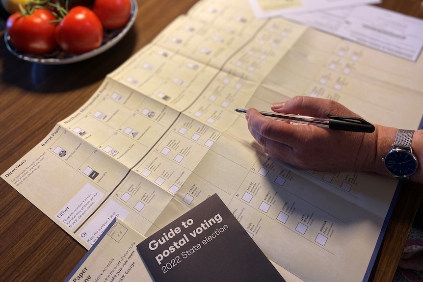 A hand holding a pen about to fill out a ballot paper on a kitchen table.