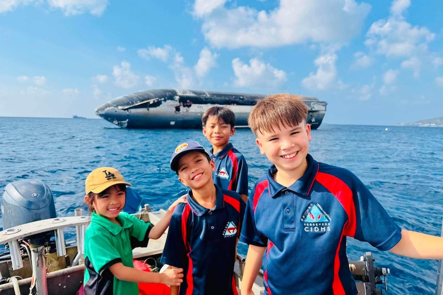 A group of young kids smile from the bow of a boat in front of a rocket.