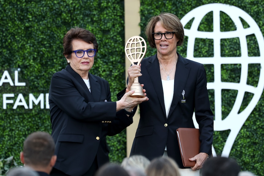 Tennis great Billie Jean King (left) stands next to broadcaster Mary Carillo (right) holding a trophy at a Tennis Hall of Fame