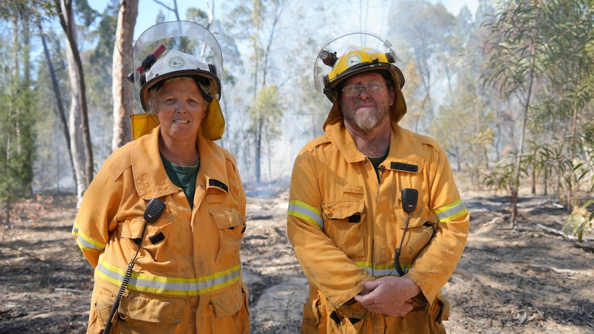 Two people wearing firefighting PPE, smoke behind them from a hazard reduction burn