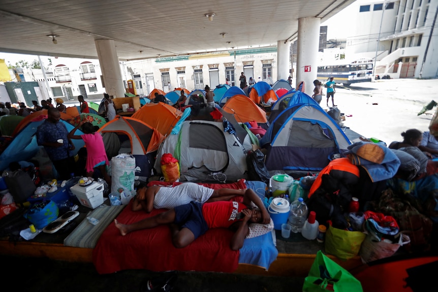 A cluster of tents sit in an abandoned petrol station, with people sprawled on the floor. 