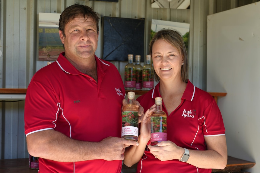 Man and woman in red uniform shirts holding bottles of clear alcohol and smiling